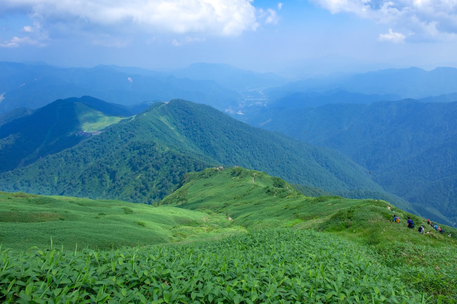 緑の山脈稜線を通る登山道と霞む遠山、青空と雲