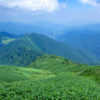 霞がかかる水上の街を望む登山道の稜線を歩くハイカーの写真