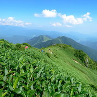 霞がかる稜線と登山道を歩む登山者たちの山岳風景の写真