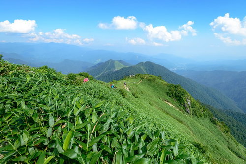 霞がかる稜線と登山道を歩む登山者たちの山岳風景