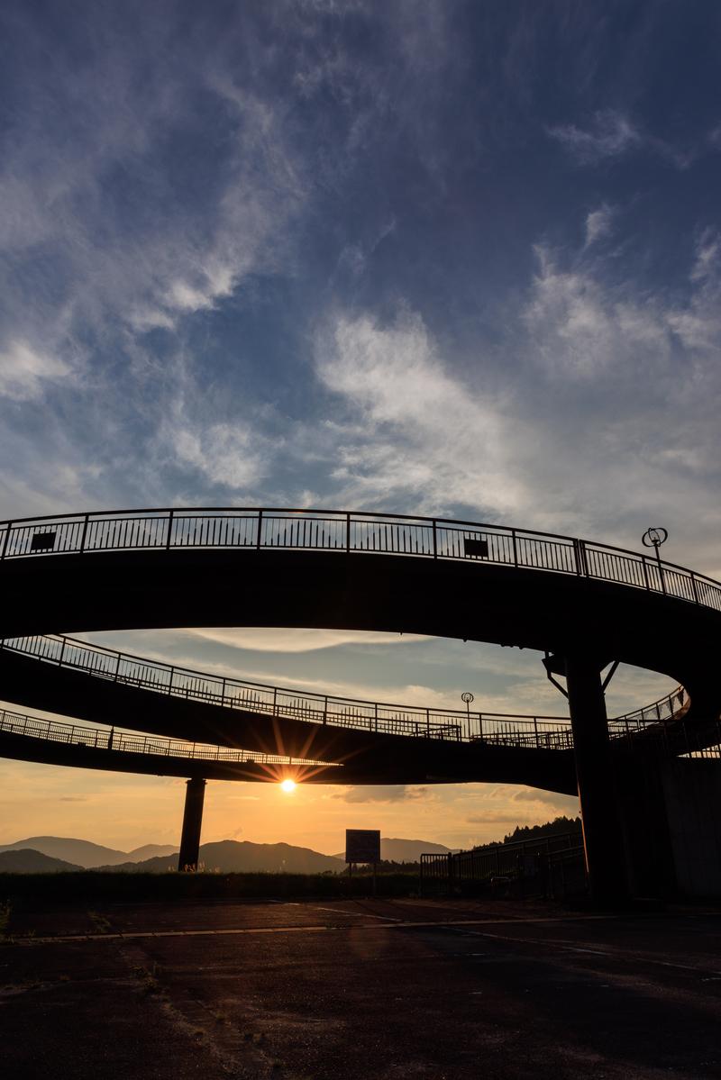 天地人橋の円形歩道橋越しに夕日が沈み、空が黄金色に染まる夕焼けの風景