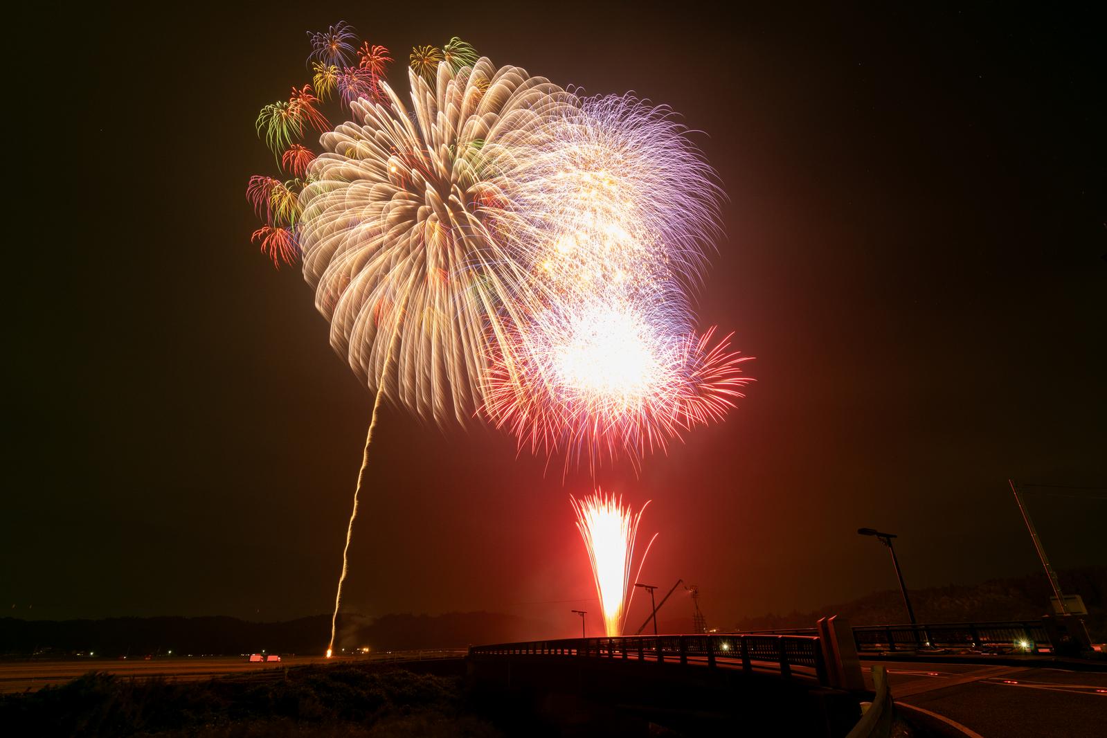 浅川町の花火大会で打ち上がる金色とピンク色の大輪の花火と赤い筒状の光