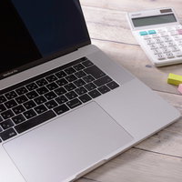 スリープ中のノートPCとキーボード、文房具が置かれたデスクの写真