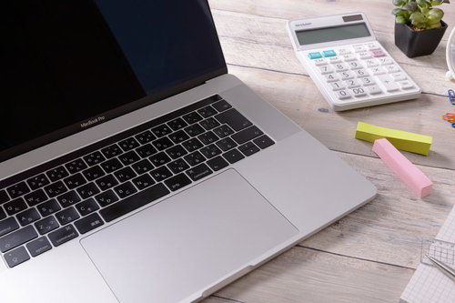 スリープ中のノートPCとキーボード、文房具が置かれたデスク