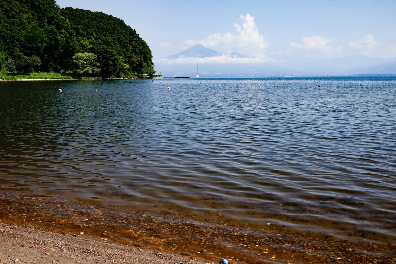 秋山浜から見た猪苗代湖と磐梯山。砂浜の波打ち際と青い水面、遠方に雲がかかった山が見える