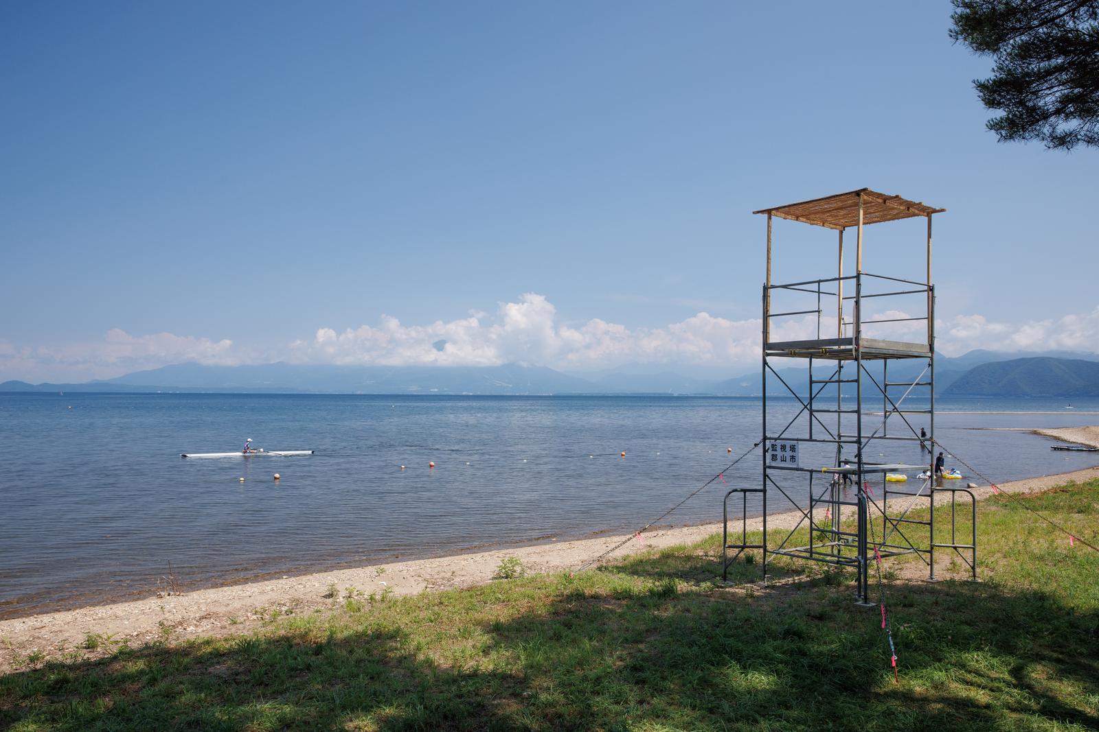 猪苗代湖畔の砂浜に立つ鉄骨製の監視塔と夏の浜辺風景