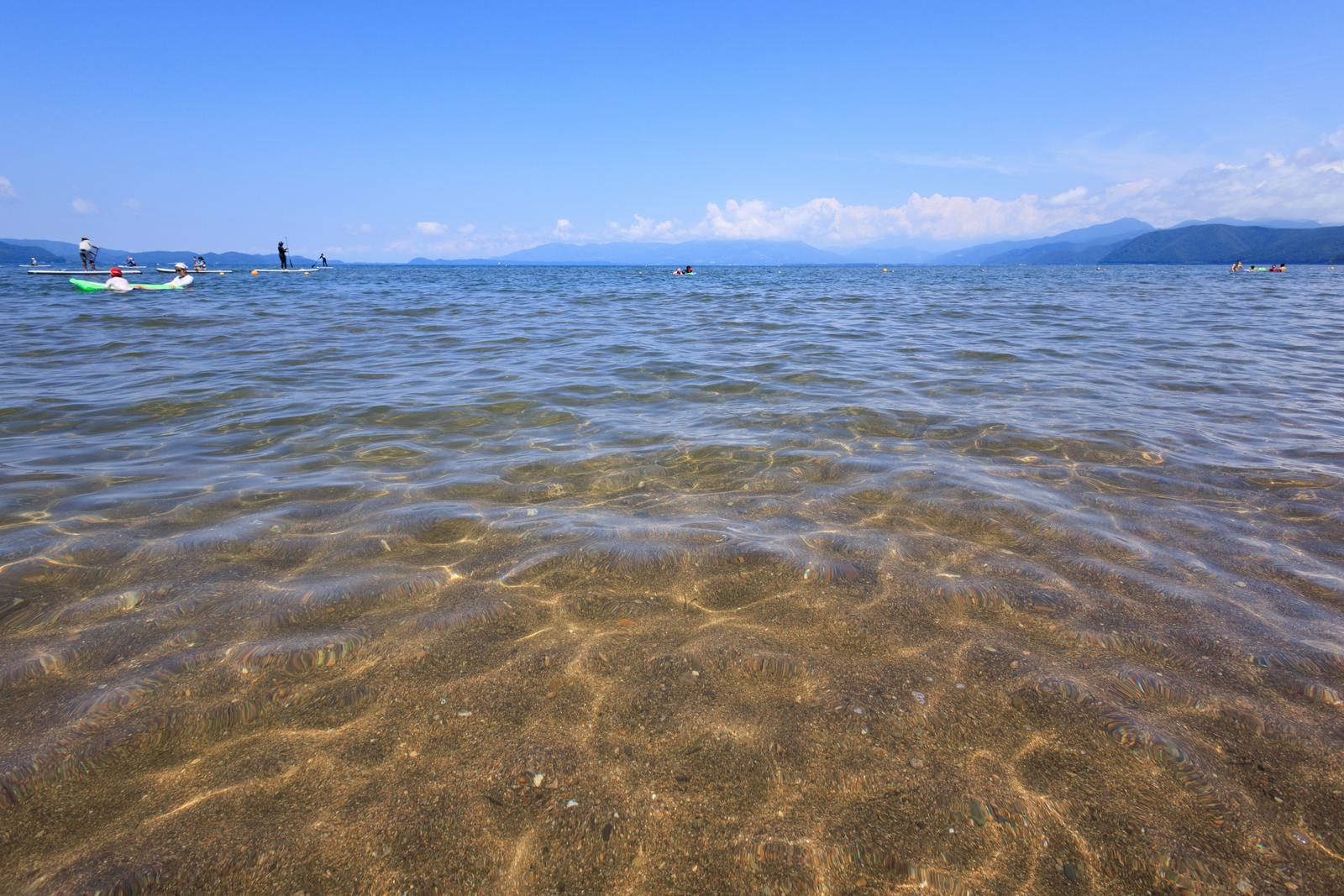 透明な水で砂底が見える猪苗代湖の浅瀬と遠くの山並み