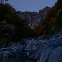 夕暮れ時の薄暗い一ノ倉沢渓谷の河原と岩壁の写真