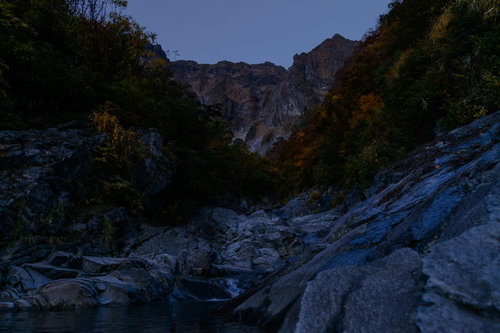 夕暮れ時の薄暗い一ノ倉沢渓谷の河原と岩壁