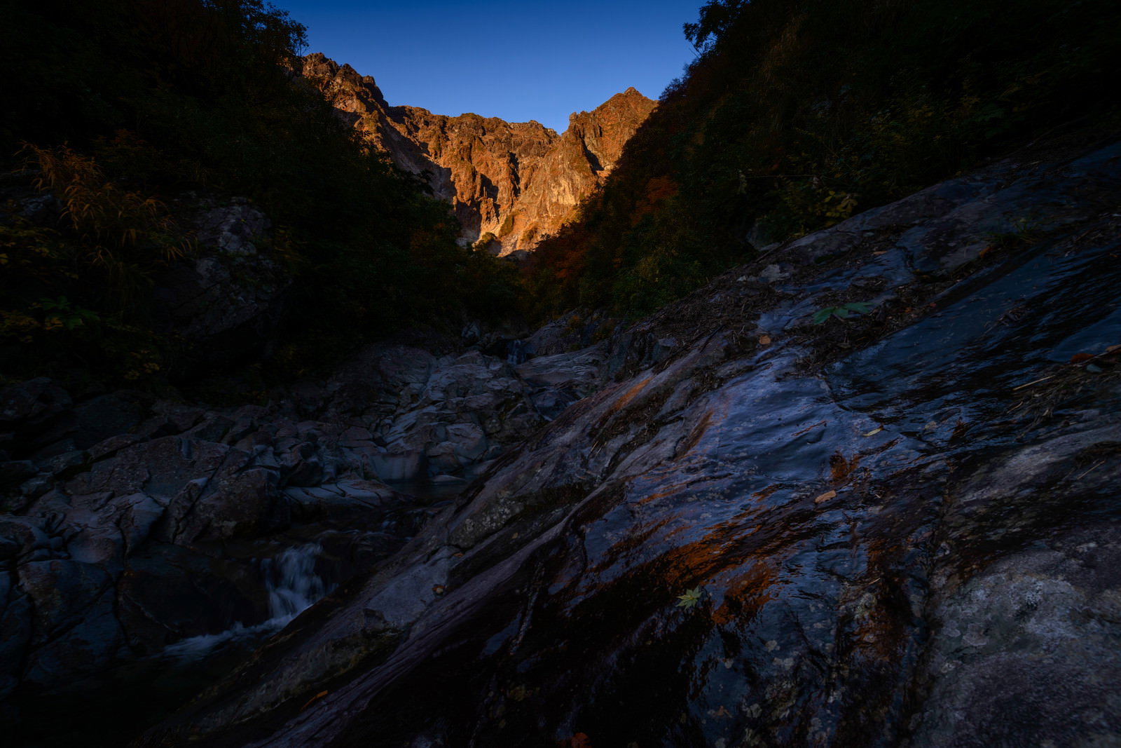 Rock walls glowing in the orange light of the setting sun, with the shadowed riverbed in the foreground