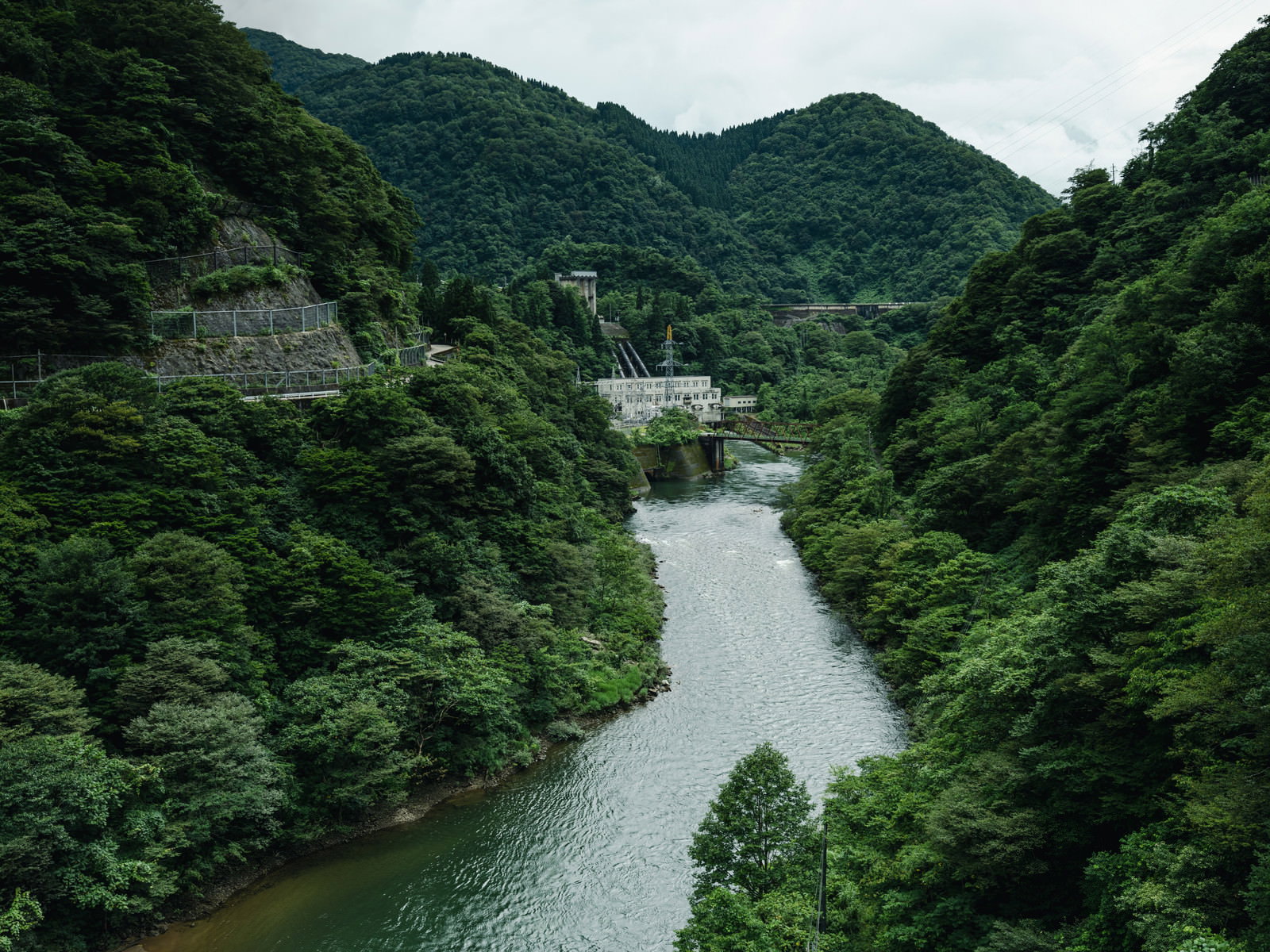 深い緑の山々に囲まれた峡谷を静かに流れる川と遠方の橋