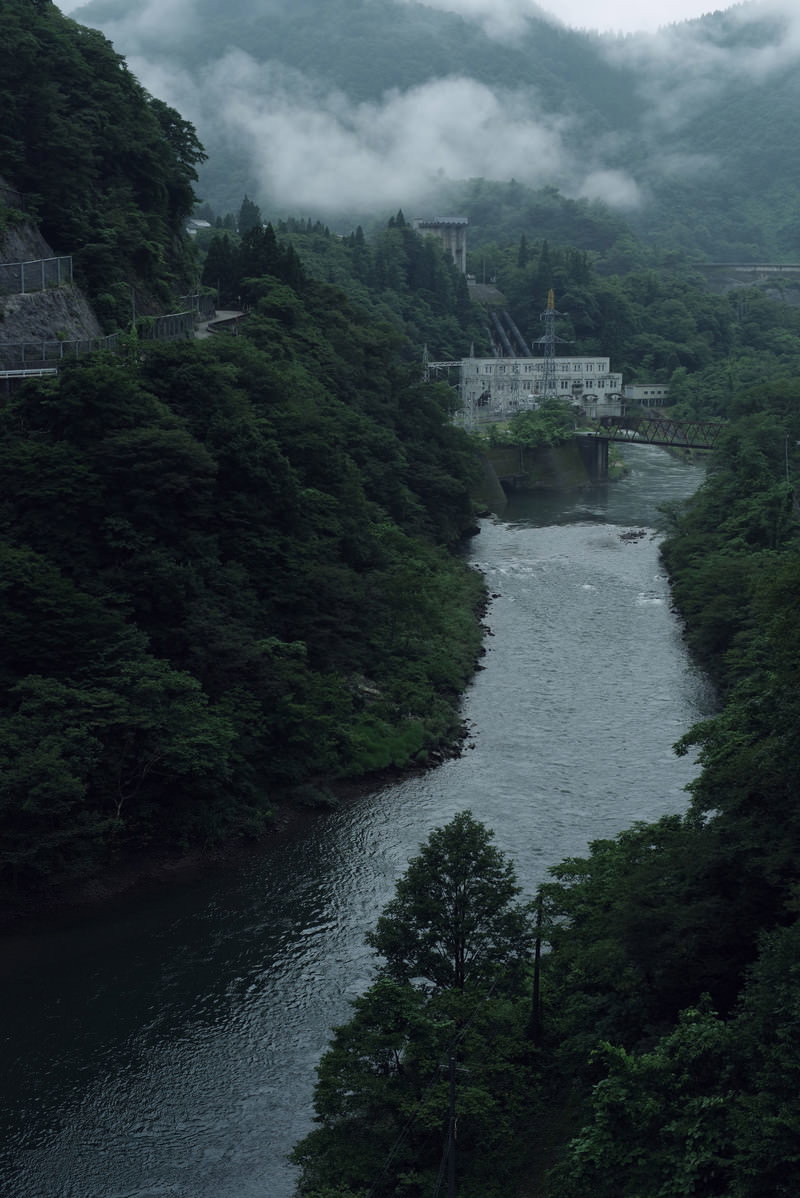 霧に包まれた山間の峡谷を流れる川と橋、ダムが見える朝の風景