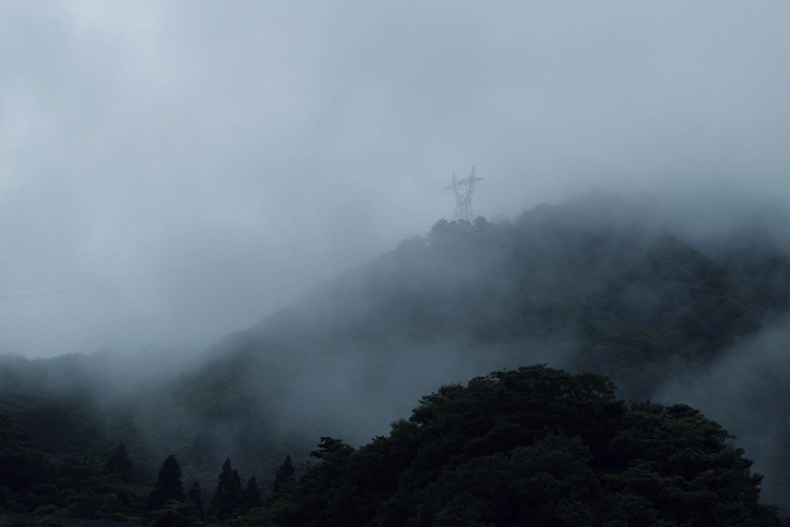 濃霧に包まれた山間部に立つ鉄塔の風景