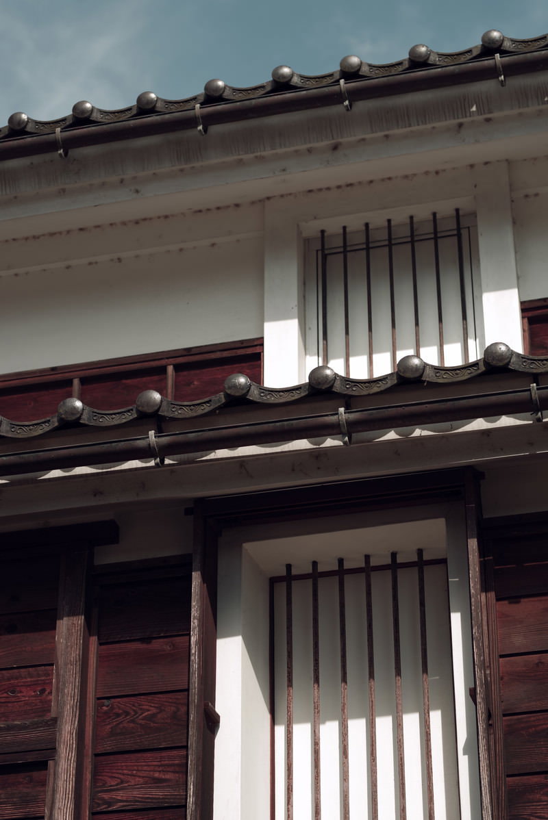 富山県南砺市の土蔵。黒い瓦屋根と赤褐色の梁、白い壁に縦格子の窓が並んでいる