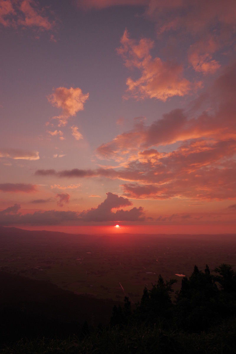 夕焼け色の雲が広がる空と山のシルエットが見える散居村の風景