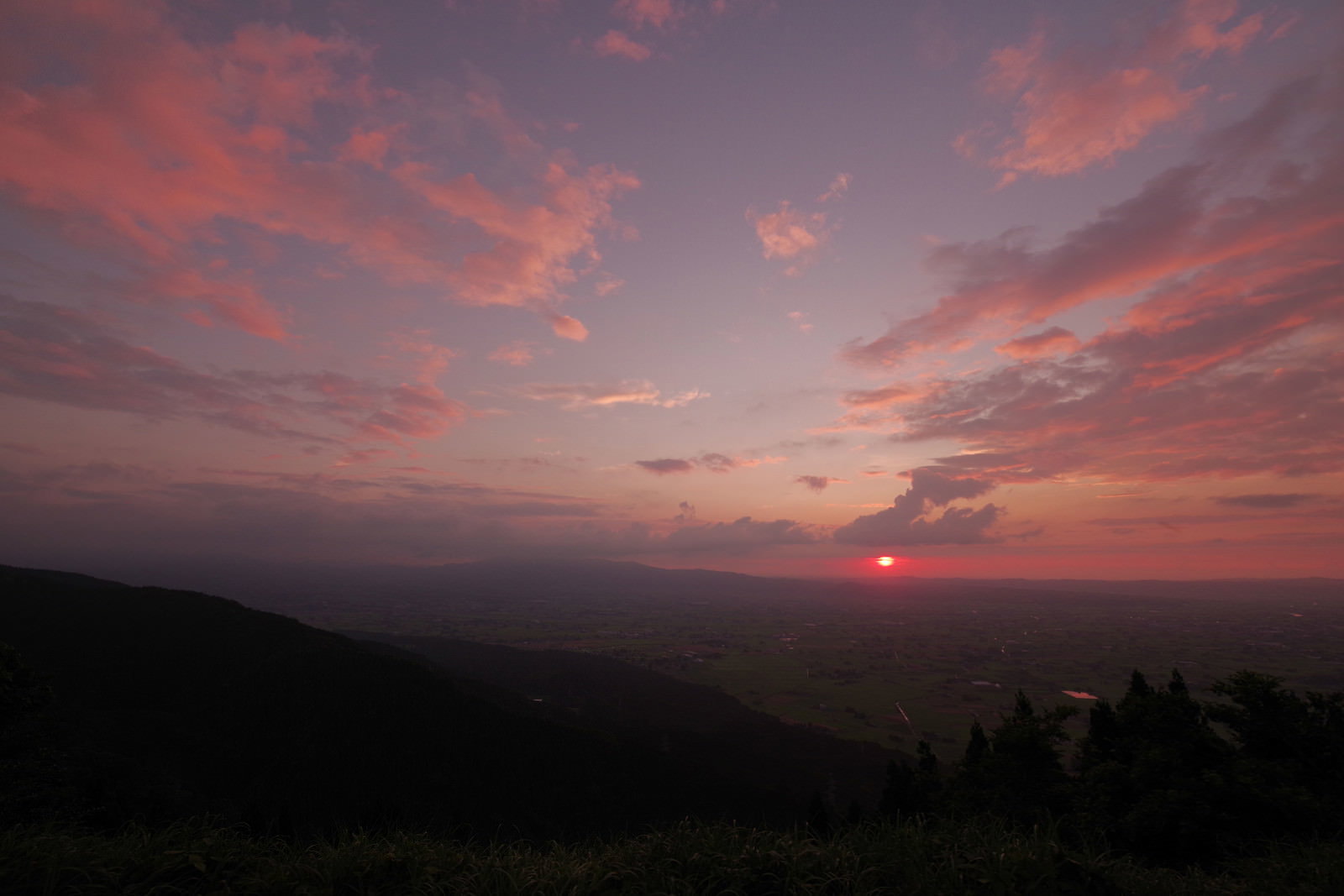 夕焼け空の下に広がる散居村の風景、オレンジとピンクの雲と山のシルエット