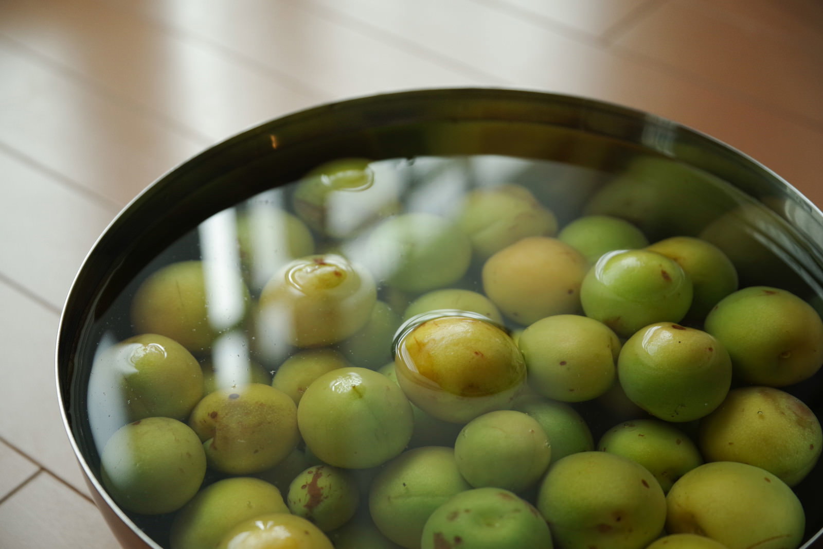 鍋の中で水に浸されてアク抜きをしている緑色の青梅