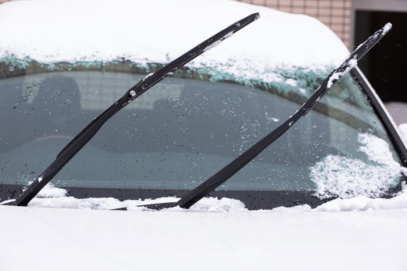 A car with its windshield wipers raised on a snowy windshield