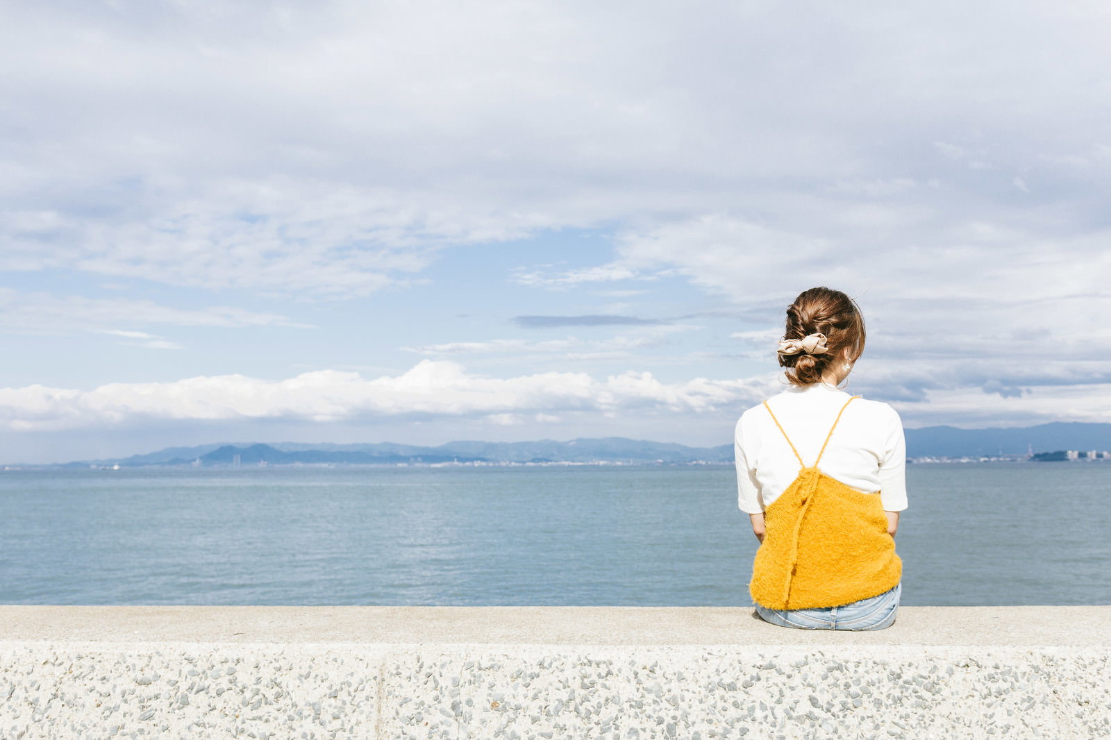 埠頭に座り海を眺める女性の後ろ姿