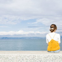 埠頭に座って海を眺める女子の後ろ姿の写真