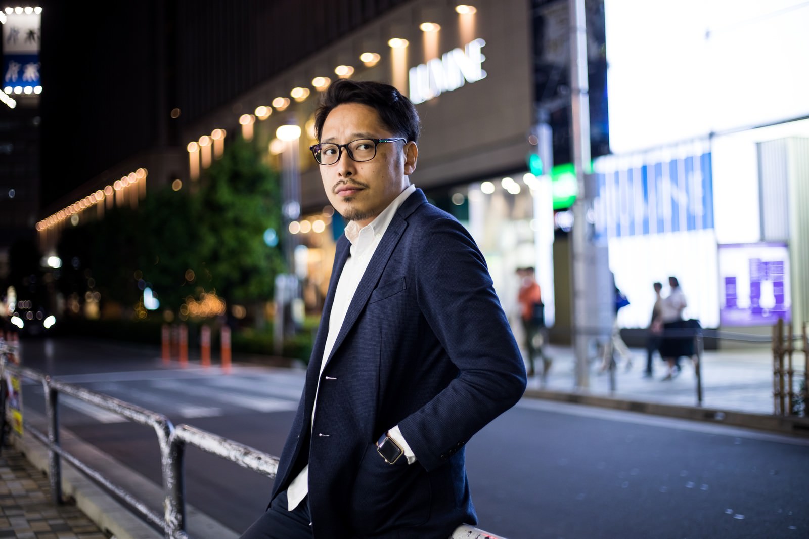 夜の駅前で待ち合わせをするスーツ姿の緊張したアラサー男性［モデル：ゆうせい］