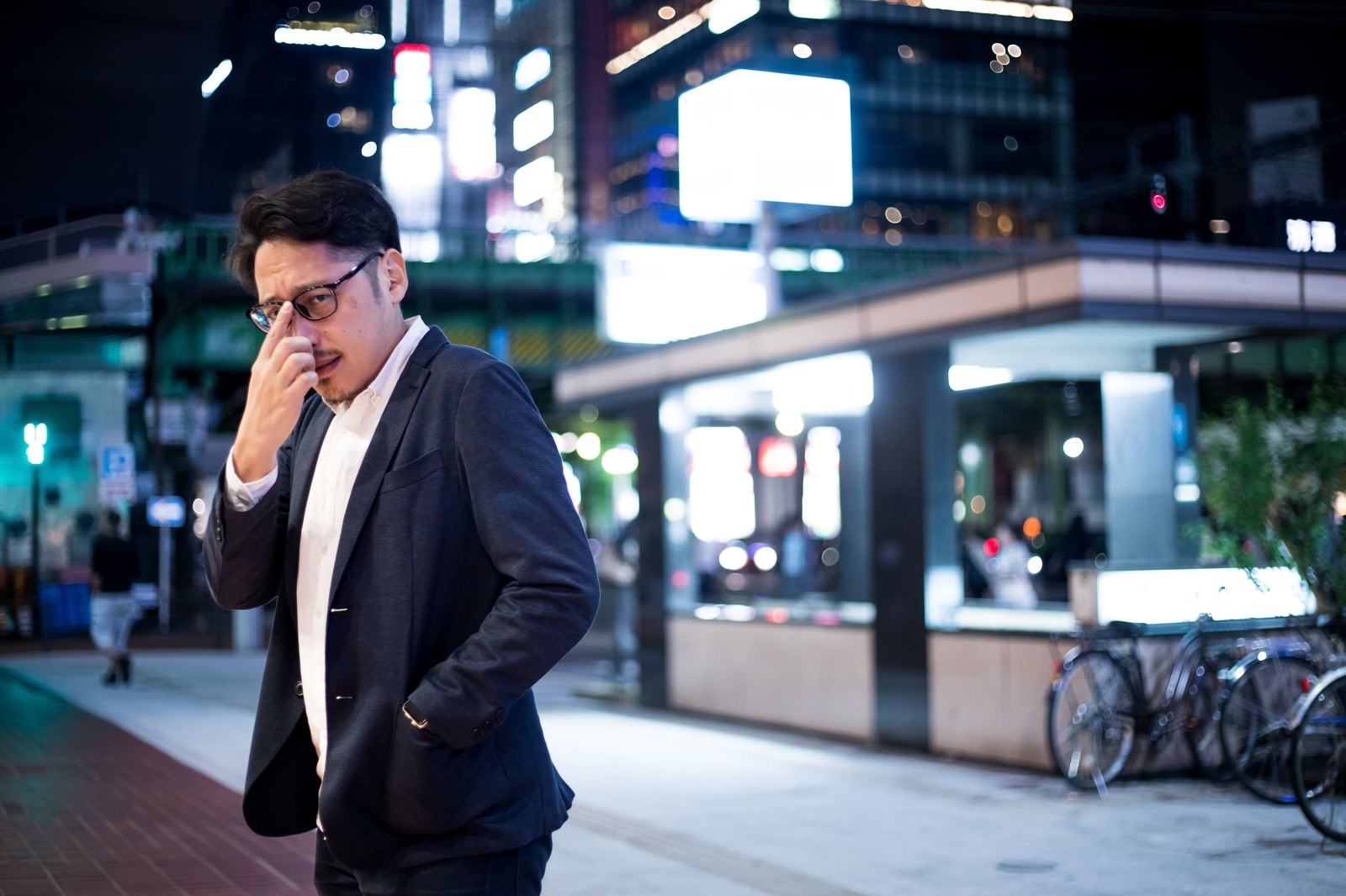 夜の街でスマートフォンを見ながら立つスーツ姿の男性［モデル：ゆうせい］