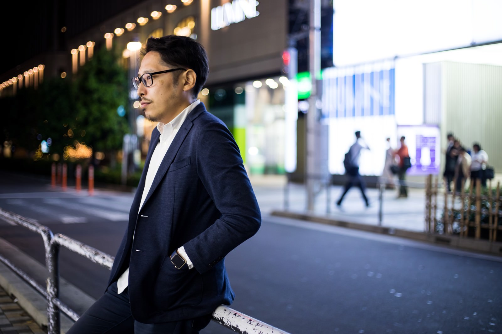 夜の駅前で待ち合わせをするスーツ姿の男性が立っている様子［モデル：ゆうせい］