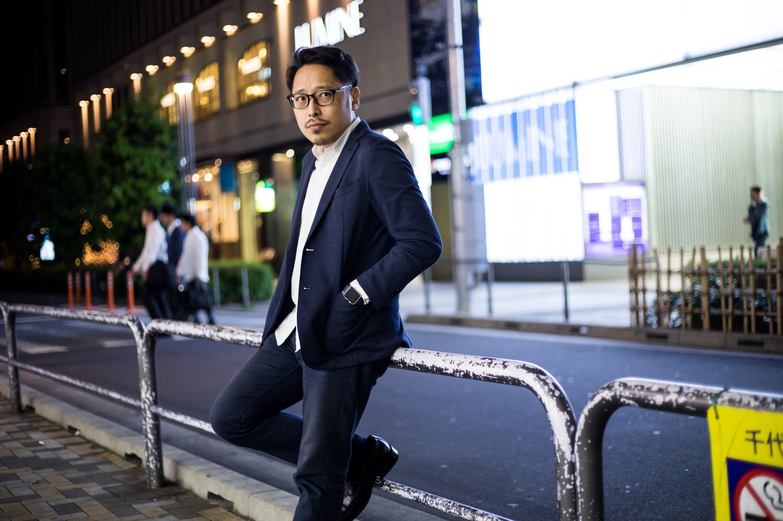 夜の駅前で待ち合わせをするスーツ姿の男性［モデル：ゆうせい］