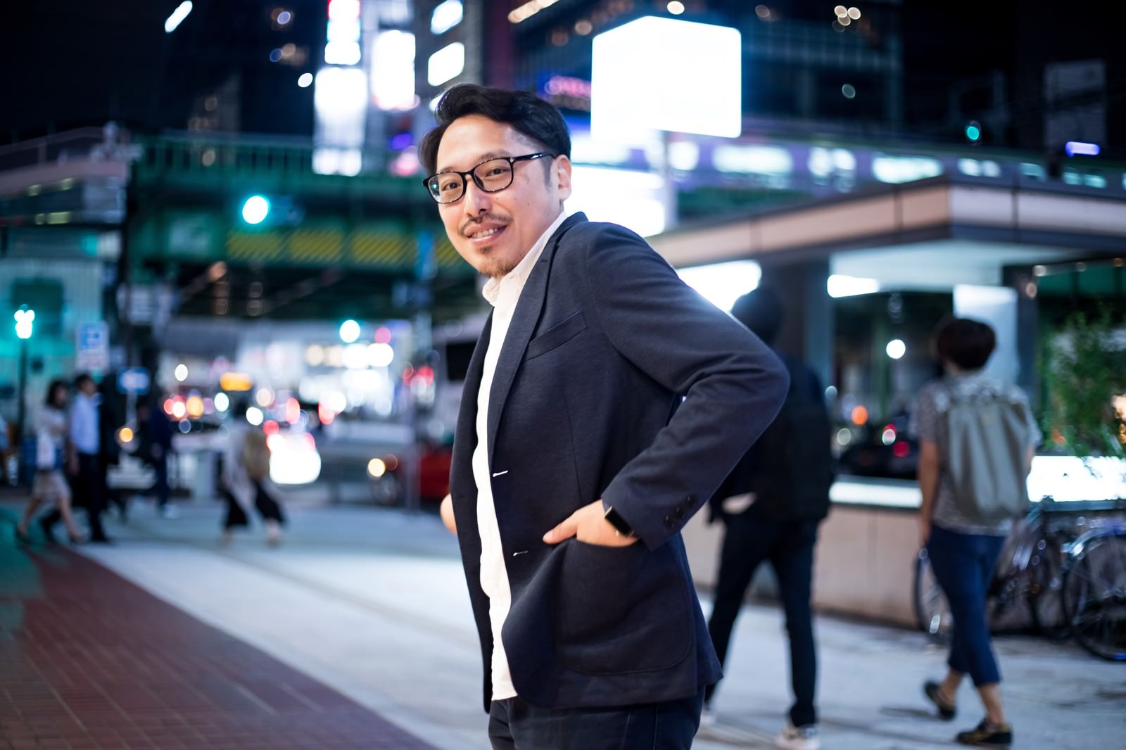 夜の街角で振り返るスーツ姿の眼鏡をかけた男性［モデル：ゆうせい］