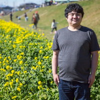 菜の花畑で春の記念撮影をする笑顔の若い男性の写真
