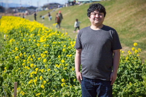 菜の花畑で春の記念撮影をする笑顔の若い男性
