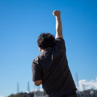 独り屋外で気合を入れてビクトリーポーズをする男性の後ろ姿の写真