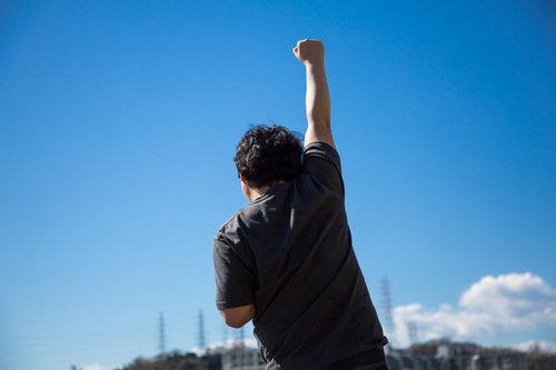独り屋外で気合を入れてビクトリーポーズをする男性の後ろ姿