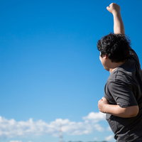 青空の下で両腕を上げて叫ぶ成功を喜ぶ男性の写真