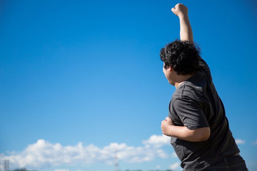 青空の下で両腕を上げて叫ぶ成功を喜ぶ男性