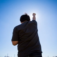 太陽に向かって拳を高々とあげる後ろ姿の男性の写真
