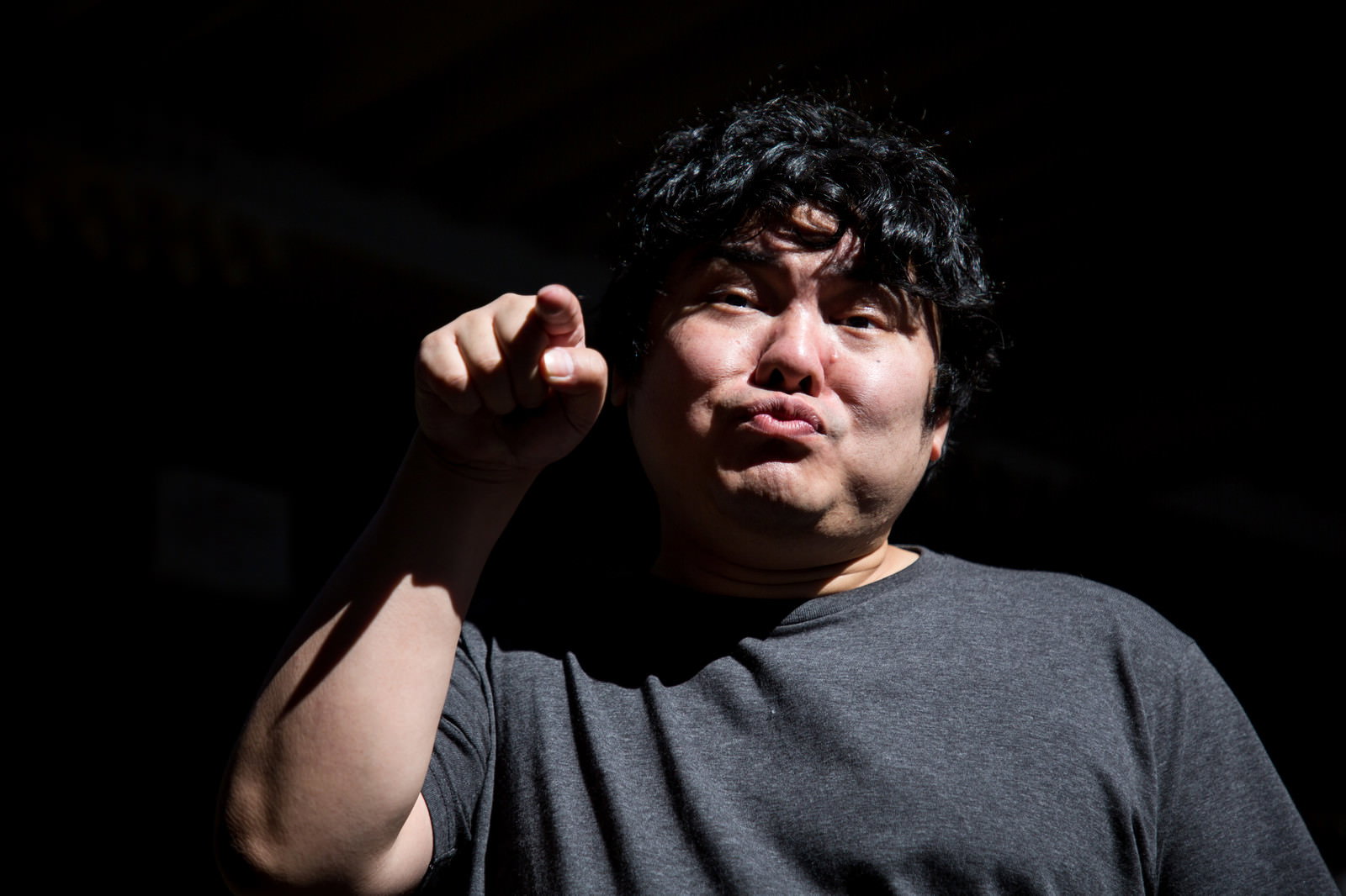 黒い背景で右手の人差し指を前に突き出してあざ笑う男性［モデル：段田隼人］