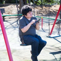 公園のブランコでスマートフォンを操作する男性の写真