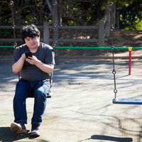 本日の営業は終了しました...っと、公園のブランコでスマホを見る男性の写真