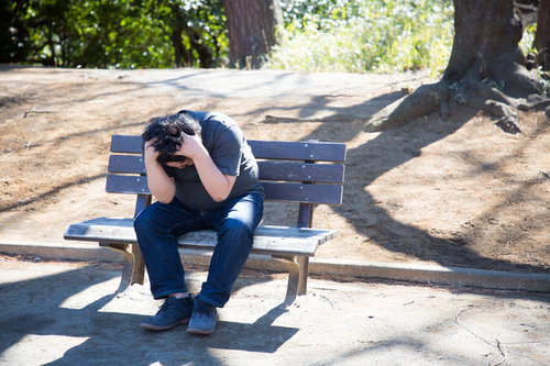 公園のベンチで頭を抱えて絶望する男性の屋外ライフスタイル