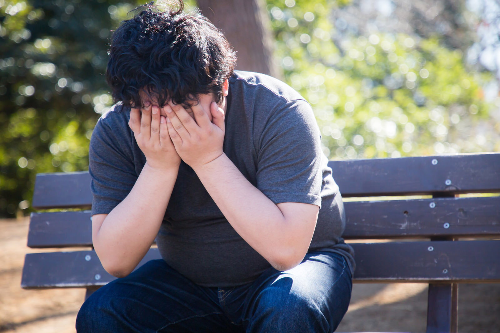 公園のベンチで頭を両手で抱えて悩んでいる男性［モデル：段田隼人］