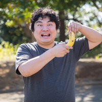 バナナを持つ男性の明るい笑顔、紺シャツで屋外ポートレートの写真