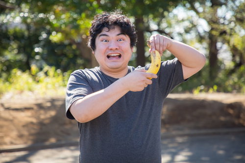 バナナを持つ男性の明るい笑顔、紺シャツで屋外ポートレート