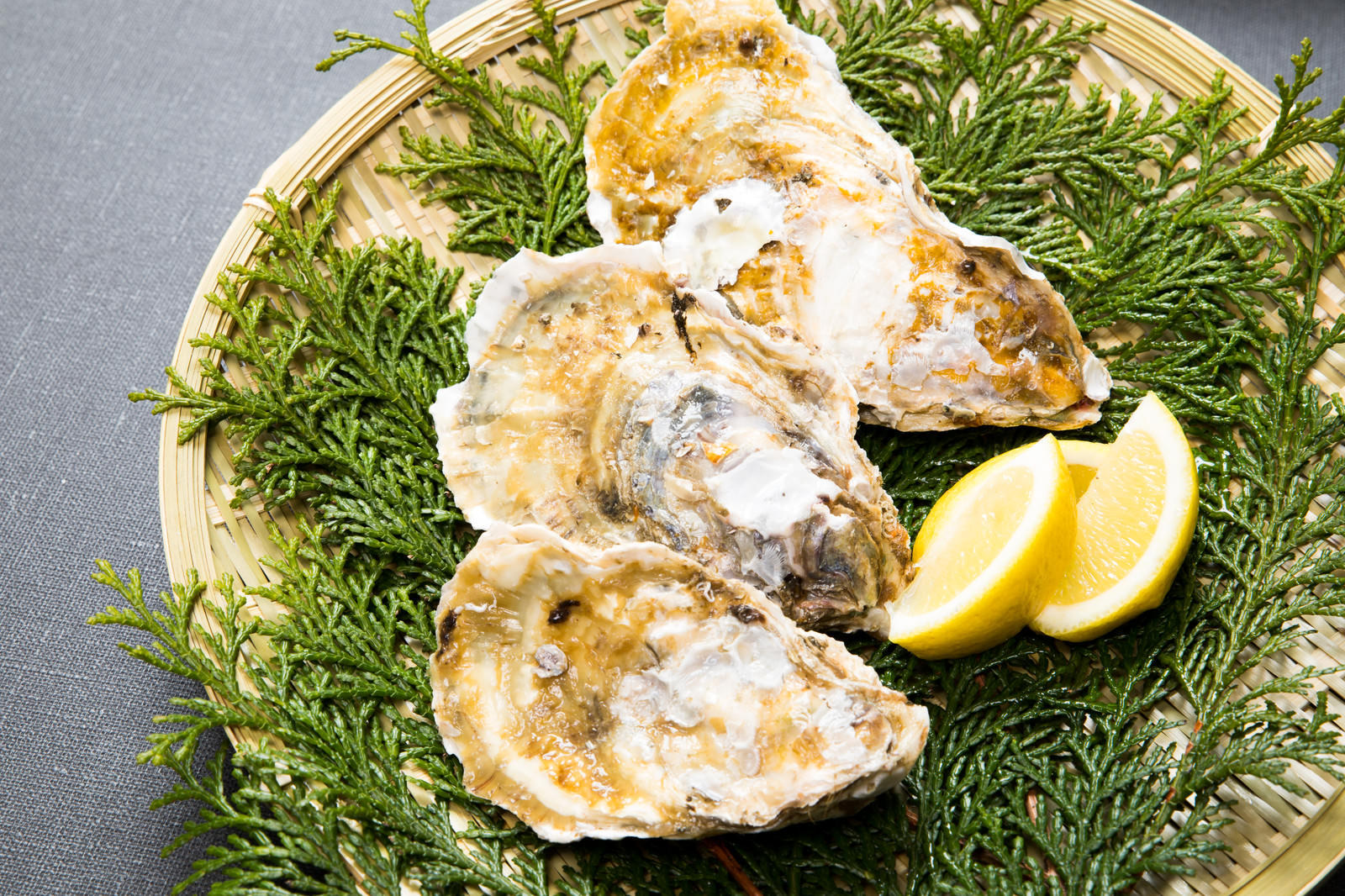 ヒノキの葉の上に盛り付けられた殻付きの恵比須牡蠣3個とレモン