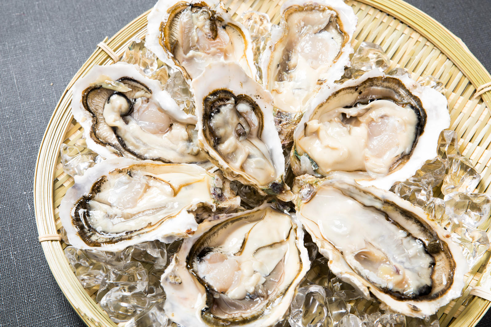 竹ざるに氷と共に盛られた生牡蠣8個。貝殻が開き、白い身が露出した状態