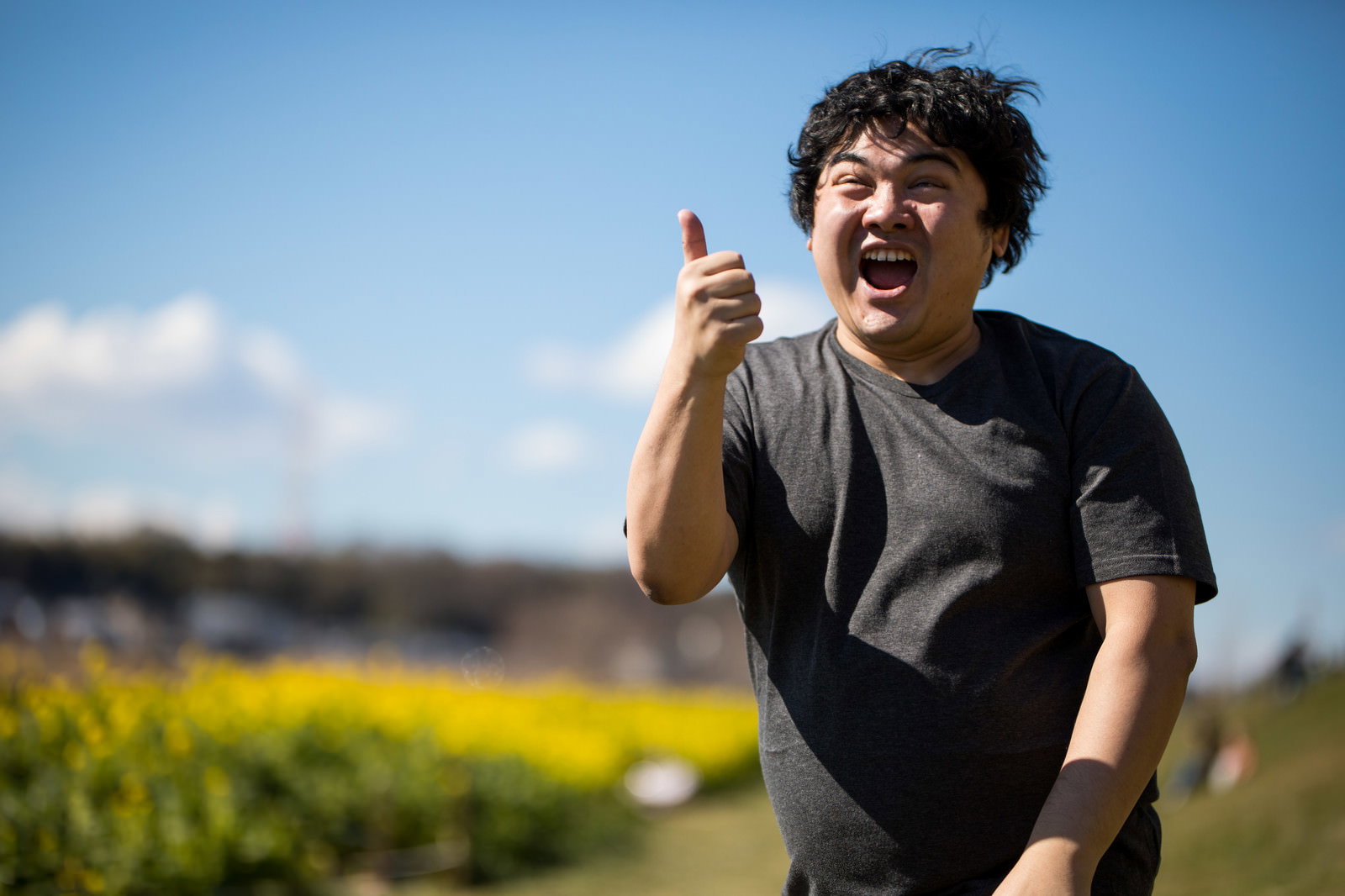 菜の花畑でサムズアップして笑う男性［モデル：段田隼人］