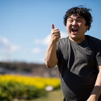 春の菜の花畑で両手でいいねをする男性の笑顔の写真