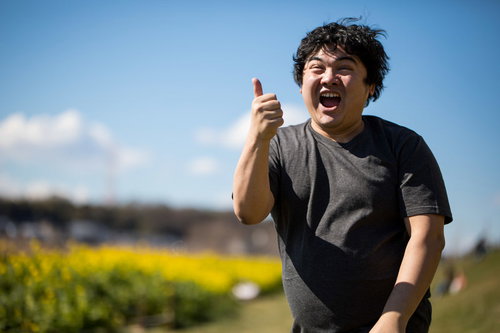 春の菜の花畑で両手でいいねをする男性の笑顔