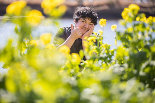 菜の花畑で親指を立てるサムズアップポーズの男性