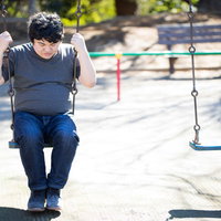 公園のブランコで一人うつむく男性の写真